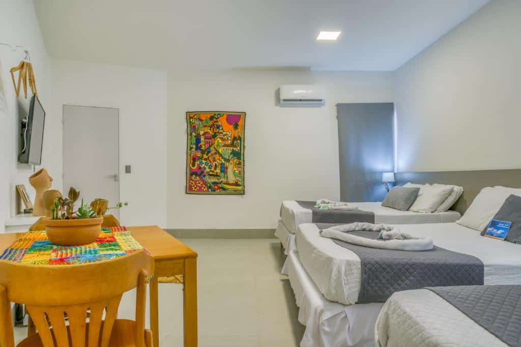 Quarto familia da Pousada Praia Pajuçara, de 30 m², com 3 camas de casal, uma mesa quadrada com duas cadeiras de madeira amarelada, ar-condicionado e TV