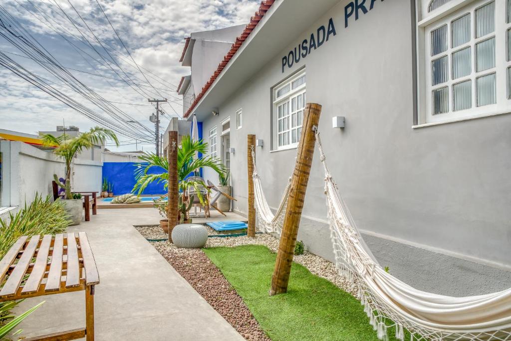 Área externa de uma das pousadas em Alagoas, com redes, bancos, piscina com almofada em volta e no lado direito tem a casa de parede cinza escrito "Pousada Praia Pajuçara"