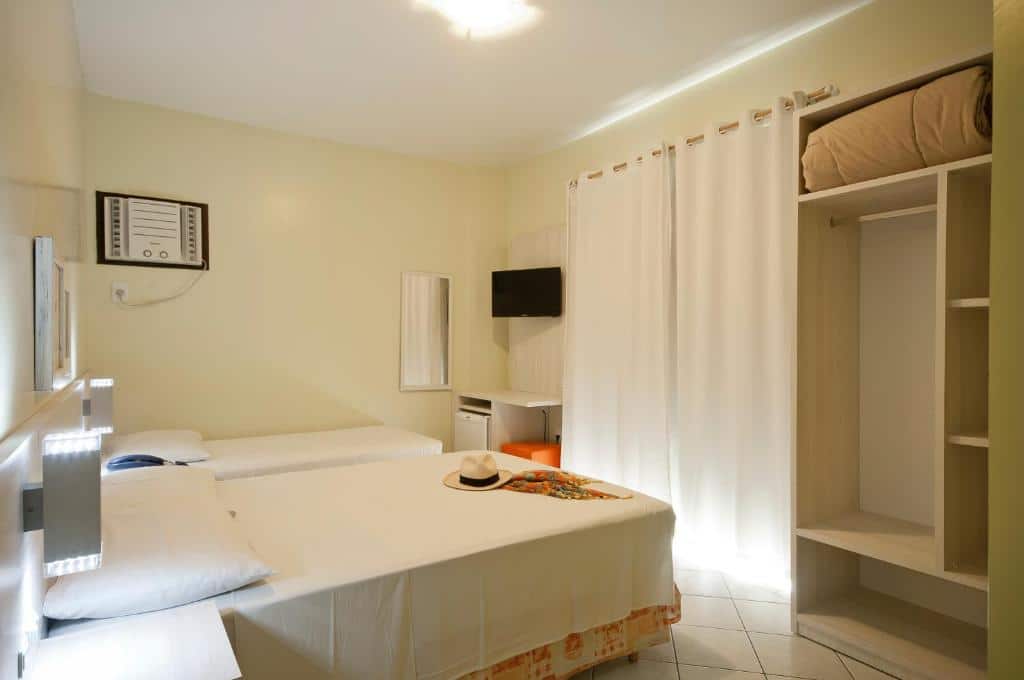Quarto Standard da Pousada Villa Atlântica, de 12 m², com uma cama de casal, uma cama de solteiro, ar-condicionado, TV, frigobar e um guarda-roupa com um edredom dentro