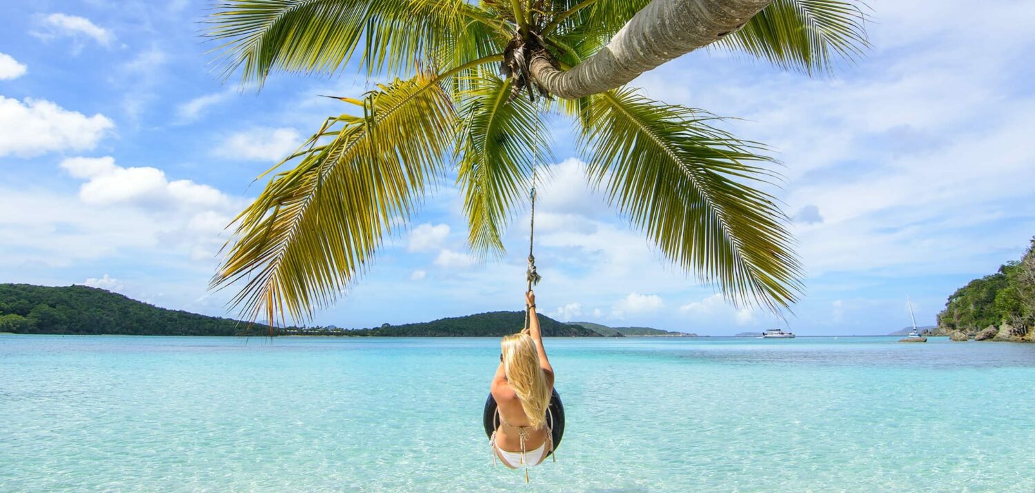 mulher em um balanço improvisado em um coqueiro que se projeta acima das águas cristalinas da Praia de Oppenheimer, em St. John, para ilustrar o post de chip celular Ilhas Virgens Americanas