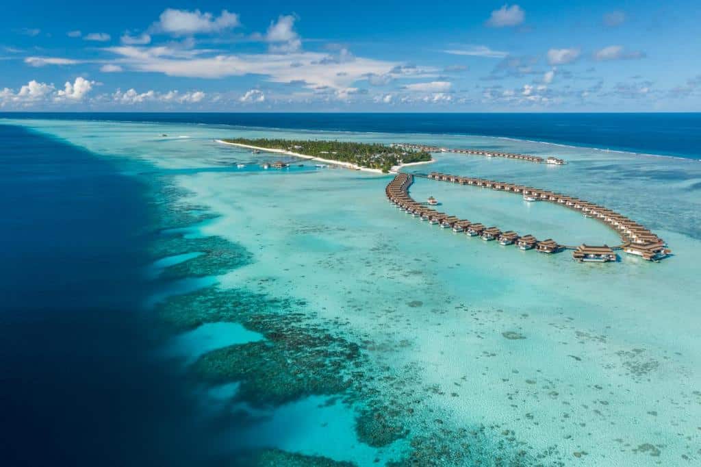Vista aérea do Pullman Maldives All-Inclusive, sendo o local localizado em uma ilha isolada com mar cristalino em volta. Há alguns bangalos flutuantes no mar