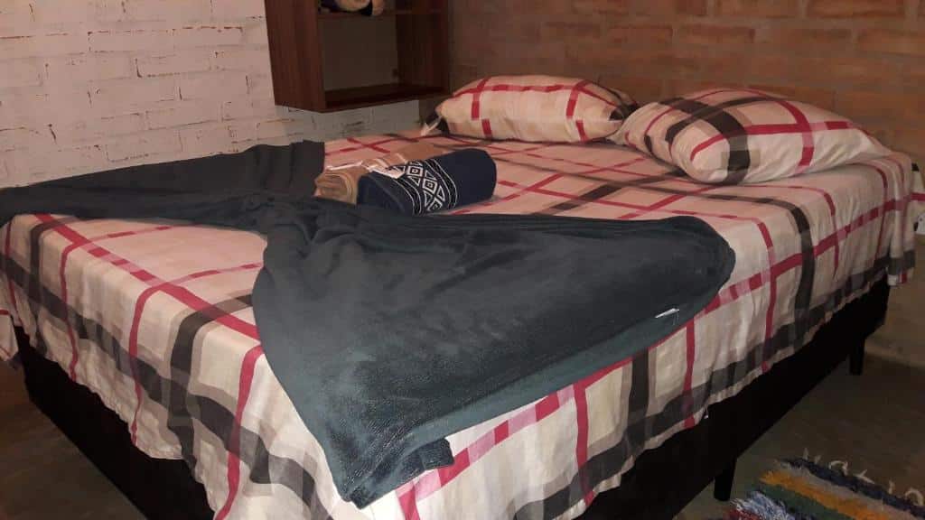 Quarto do Chalés do Alcantilado com uma cama de casal com uma manta cinza em cima da cama e duas toalhas azul  e cinza.