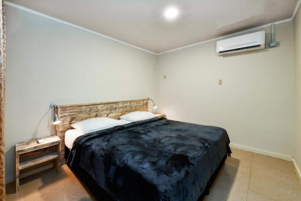 quarto do Aruba Blue Village Hotel and Apartments com uma cama de casal no centro da suíte com cabeceira de madeira e dois abajures em cada lado da cama. No canto superior direito é possível ver um ar-condicionado