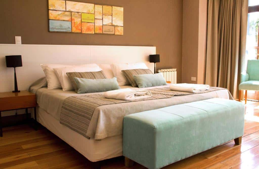 Quarto do Boutique Hotel & Spa Bosque del Nahuel com cama de casal, duas cômodas de madeira com luminárias e uma poltrona azul na beira da cama.