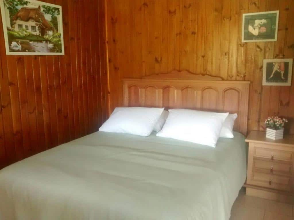 Quarto do Chalés Rincão Comprido com cama de casale do lado direto cômoda com vaso de flor rosa.