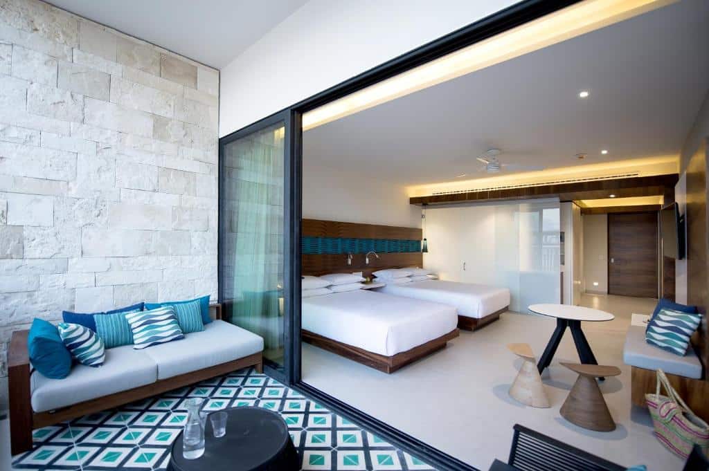 Quarto do Grand Hyatt Playa del Carmen Resort com uma ampla varanda com um sofá de dois lugares, duas camas de casal dentro da suíte, uma televisão, uma mesinha de centro e dois bancos de madeira