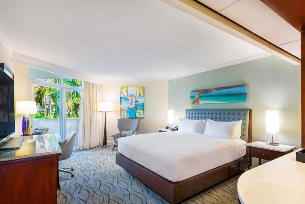 suíte do Hilton Aruba Caribbean Resort & Casino com uma grande cama de casal à direita do quarto, portas duplas e acesso ao jardim