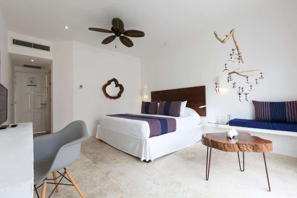 Quarto do HM Playa del Carmen com uma cama de casal, um pequeno sofá, uma mesinha de centro rústica e, um ventilador de teto que se parece com uma flor