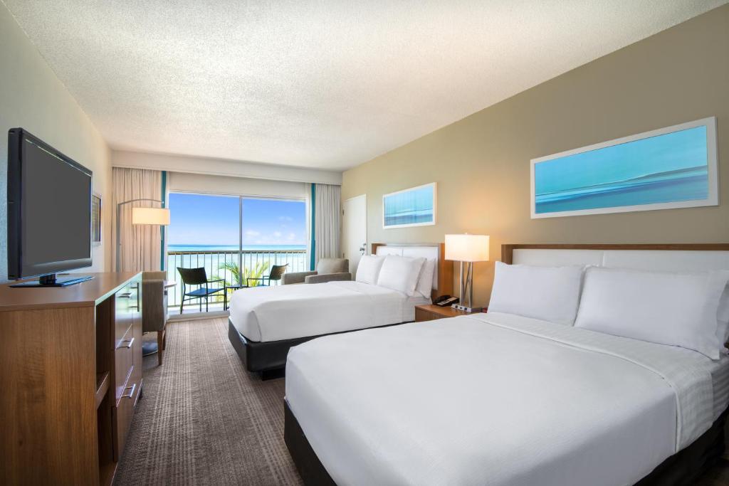 quarto do Holiday Inn Resort Aruba com duas camas de casal, uma área de estar e uma varanda particular com vista para o mar