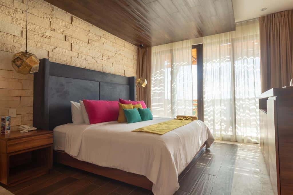 Quarto no  Hotel Beló Isla Mujeres com uma varanda, uma cômoda de madeira, uma cama de casal, o chão é de madeira e o local contra com decoração rústica