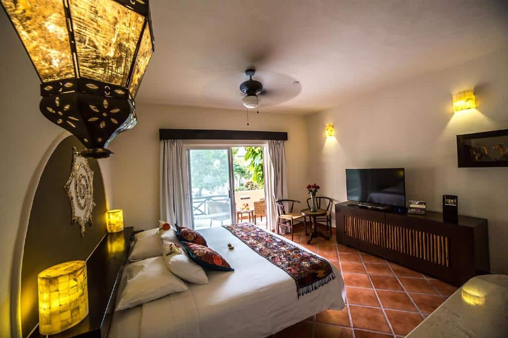Quarto do Hotel Riviera Del Sol Hotel Riviera Del Sol com uma cama de casal, uma varanda, um ventilador de teto e uma móvel de madeira com uma televisão