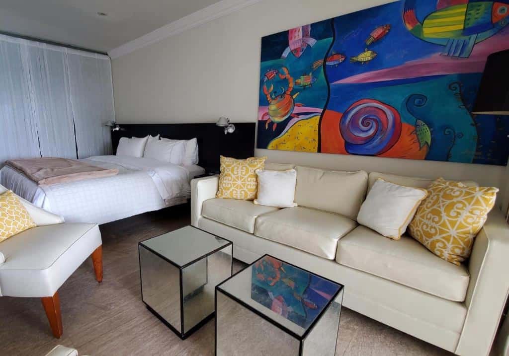 Quarto do Hotel Secreto com uma cama de casal, um sofá com três lugares, um quadro com desenhos de praia e um chão de madeira