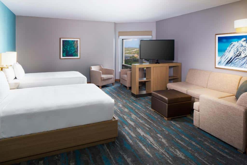 quarto acessível do hotel Hyatt Place Aruba Airport com duas camas de casal e um espaço com sala de estar, um sofá de canto com três lugares e duas poltronas, além de uma televisão de tela plana