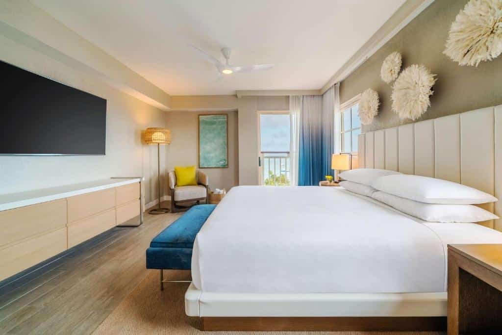 quarto do Hyatt Regency Aruba Resort & Casino com uma cama de casal à direita, uma televisão presa à parede no lado esquerdo e janelas amplas com vista para o mar