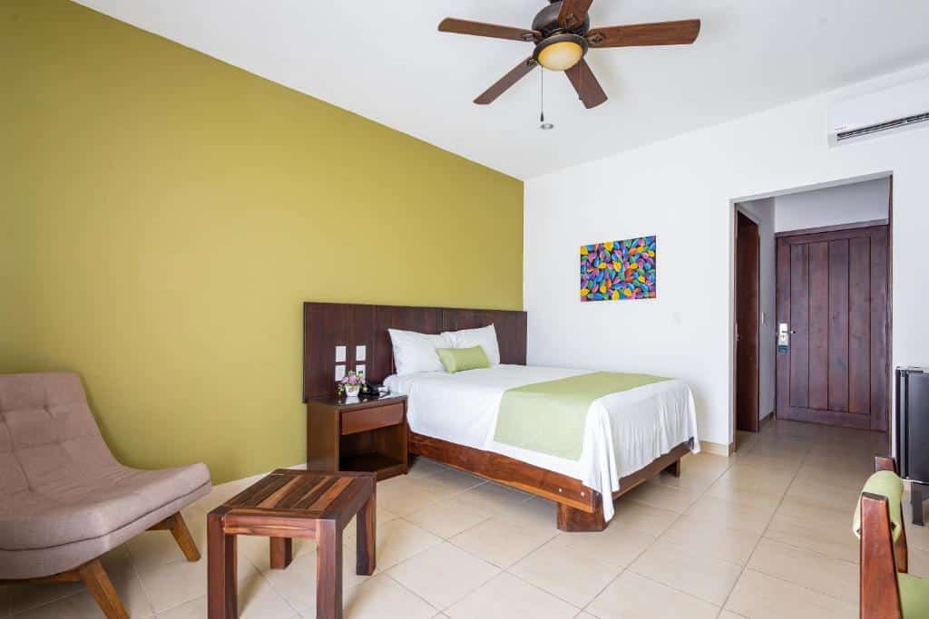 Quarto do Imperla Hotel com uma cama de casal, uma parede em tom de verde abacate, um ventilador de teto, uma poltrona e uma mesinha de cabeceira