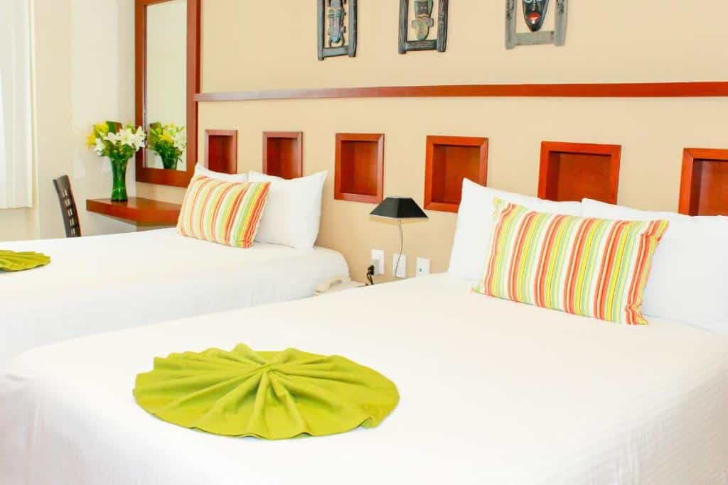 Quarto do Ixchel Beach Hotel com duas camas de solteiro, um espelho, uma pequena bancada com uma cadeira, tudo decorado em tons de branco, laranja e verde