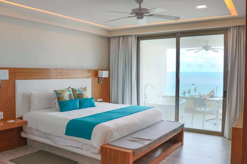 Quarto do Izla Beach Front Hotel  com uma varanda de frente para o mar e uma banheira de hidromassagem na varanda, dentro do quarto há uma cama de casal, ventilador de teto, chão de madeira e um banco de madeira, para representar hotéis em Isla Mujeres