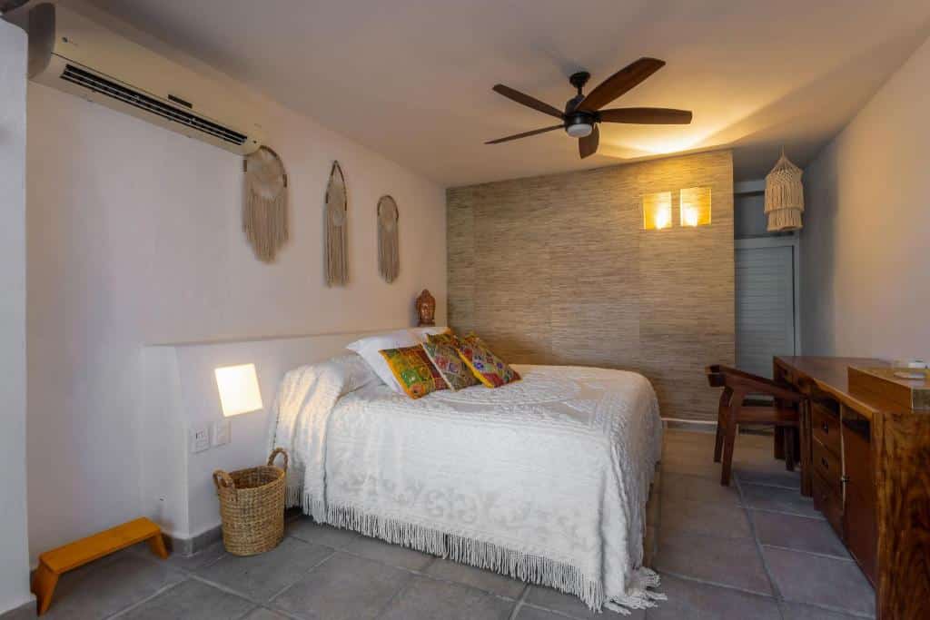 Quarto no Lotus Beach Hotel - Adults Only com uma cama de casal, um ventilador de teto e um ar-condicionado de teto, há alguns enfeites de crochê na parede, além de um móvel de madeira com uma cadeira de frente para a cama