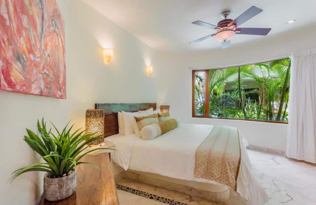 Quarto do Maya Villa Condo Hotel and Beachclub com uma ampla janela com vista para o jardim, uma cama de casal com almofadas, um ventilador de teto e alguns detalhes rústicos na decoração