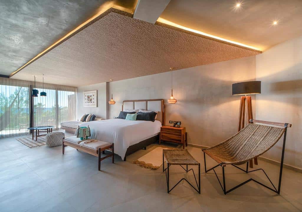 Quarto do Mvngata Boutique Hotel com cama de casal, chão de madeira, uma varanda com rede, um pequeno sofá e duas poltronas em estilo rústico, para representar hotéis em Playa del Carmen