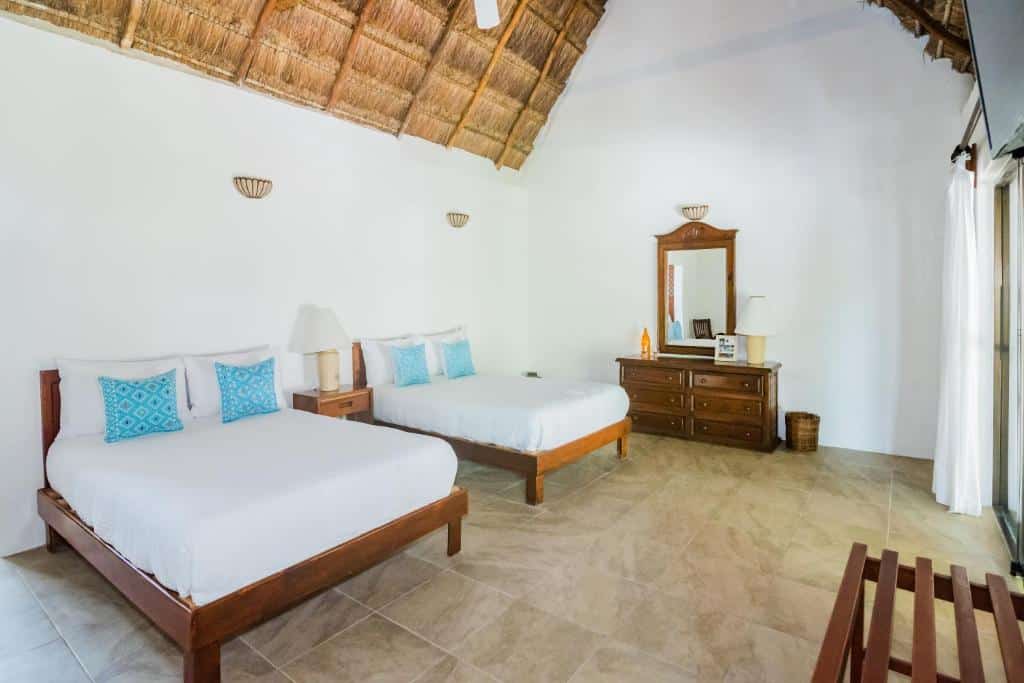 Quarto amplo do Na Balam Hotel com duas camas de casal, uma varanda, uma cômoda de madeira, um espelho e um banco de madeira