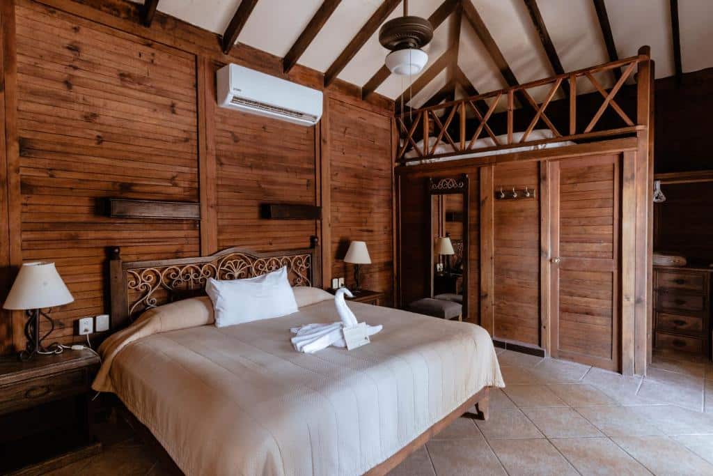 Quarto em um bangalôs de madeira do Petit Lafitte Beach Front Hotel & Bungalows com tudo decorado em madeira, uma cama de casal, um ar-condicionado de teto e dois abajures
