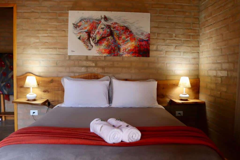 Quarto do Refúgio Horse com cama de casal, duas toalhas em cima da cama e duas cômodas com luminárias ao lado da cama.
