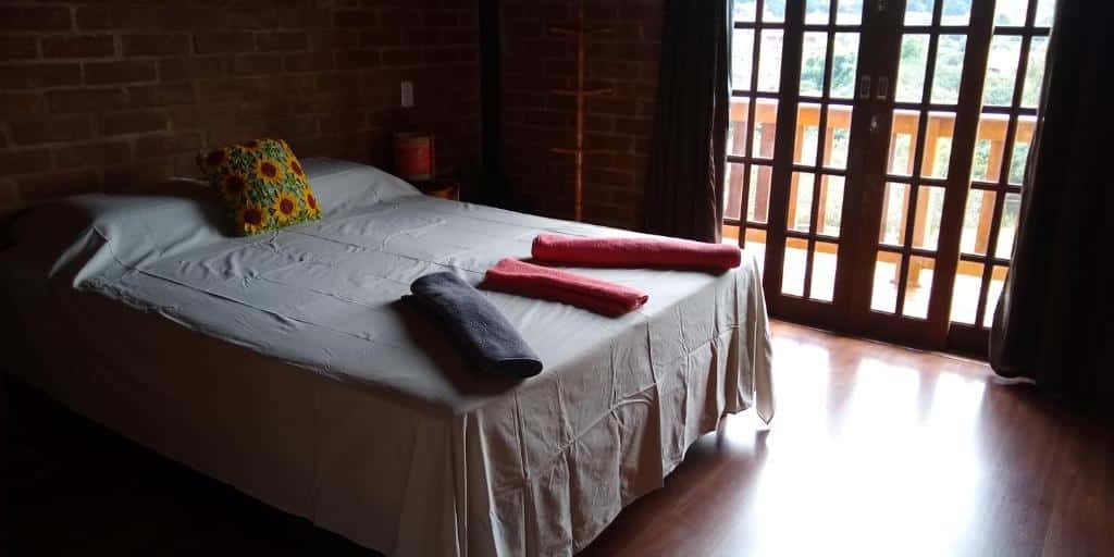 Quarto do Chalés Roma com uma cama de casal, com três toalhas em cima da cama, portas de madeira com saída para a varanda.