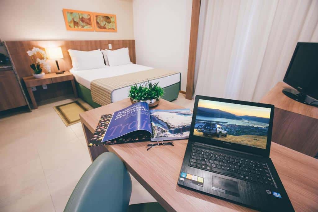 Quarto do Saint Moritz Hplus Express com uma cama de casal, uma mesinha de cabeceira com um abajur, uma televisão, uma mesa de escritório com uma cadeira giratória, para representar hotéis perto do consulado americano em Brasília