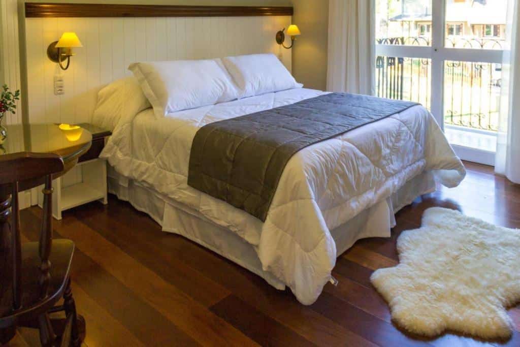 Quarto do Tri Pousada Caracol com cama de casal, duas cômodas de madeira no lado da cama, no lado direito, tem uma mesa de madeira e, no lado esquerdo, varanda com sacada.