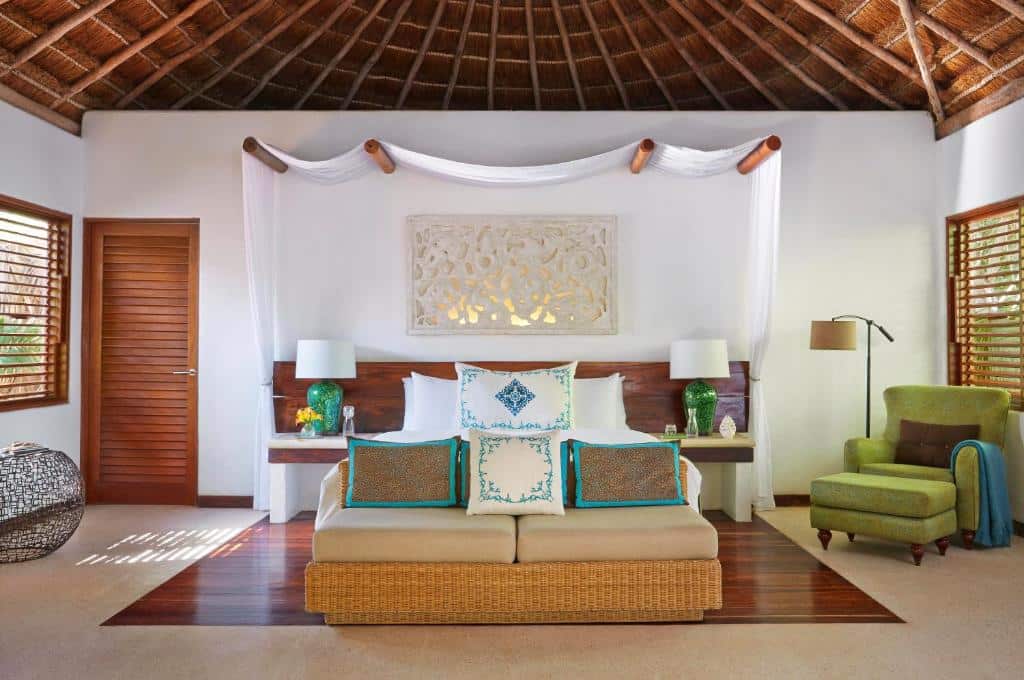 Quarto do Viceroy Riviera Maya - Luxury Resort com uma cama de casal, uma poltrona, um sofá de dois lugares e alguns itens de decoração em madeira