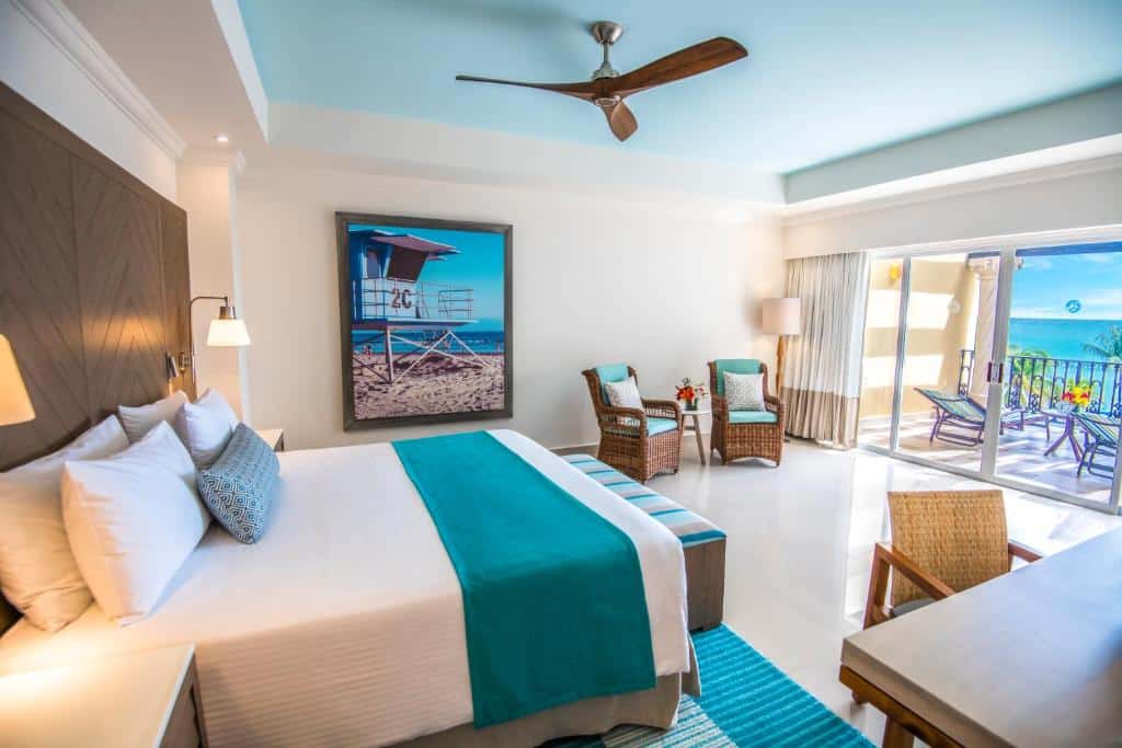 Quarto do Wyndham Alltra Playa del Carmen Adults Only All Inclusive com uma varanda dando vista para o mar, uma cama de casal, duas poltronas, uma mesa de escritório e uma cadeira