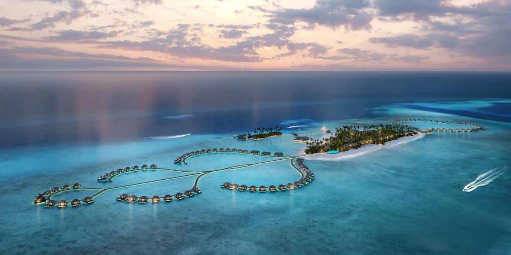 Vista aérea do Radisson Blu Resort, com bangalôs flutuantes no mar e duas pequenas ilhas ao meio.O mar tem um tom mais cristalino nas regiões próximas da ilha e um tom mais escuro nas áreas mais distantes