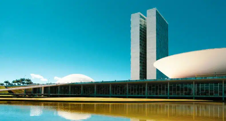 Praça dos Três Poderes em Brasília, um extenso lago com construções arquitetônicas em formato de cuba e duas torres logo atrás