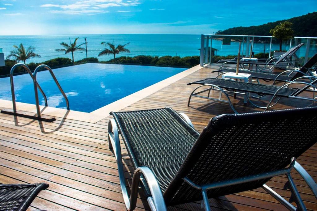 Piscina de borda infinita do Reserva Praia Hotel, em Balneário Camboriú, com mar azulado no fundo e ao lado da piscina há um deck de madeira com espreguiçadeiras espalhadas