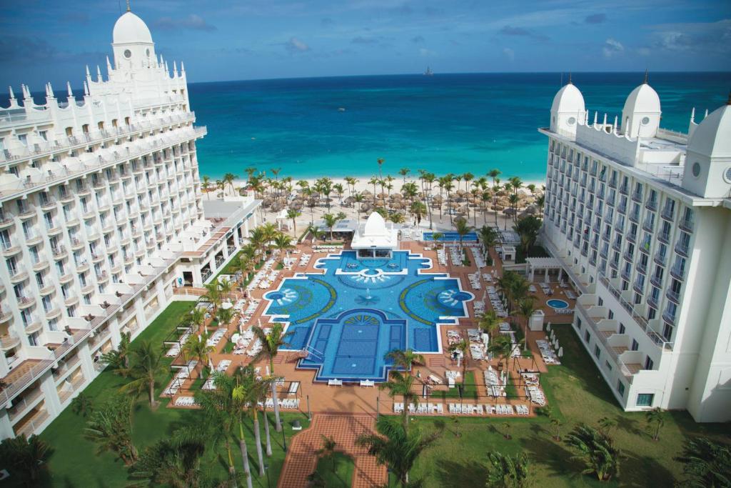 vista area do Riu Palace Aruba com dois prédios brancos à esquerda e à direita, uma grande piscina no centro e ao fundo o mar com a praia e alguns coqueiros