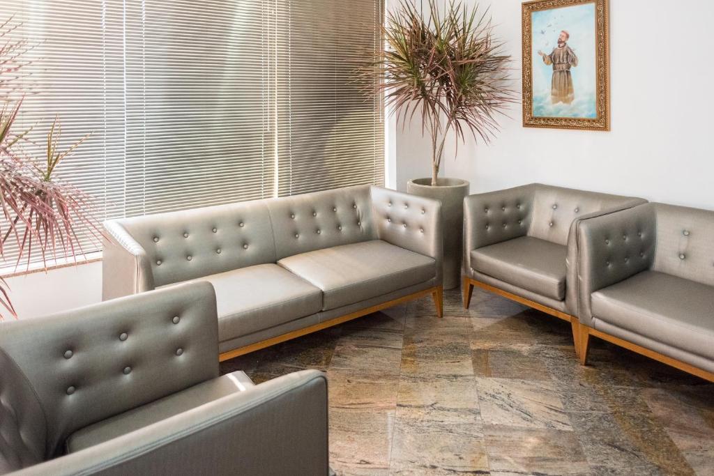 Sala da recepção do Holambra Garden Hotel com sofás de cores pratas e janelas ao fundo com cortinas de persiana, e um vaso de planta no meio. Representa hotéis em Holambra.