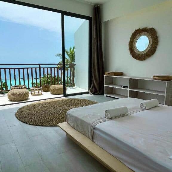 Interior da suíte com vista do mar do Samura Panorama Guest House, de 35 m², com cama de casal, tapete redondo rústico na frente e uma varanda com vista do mar cristalino