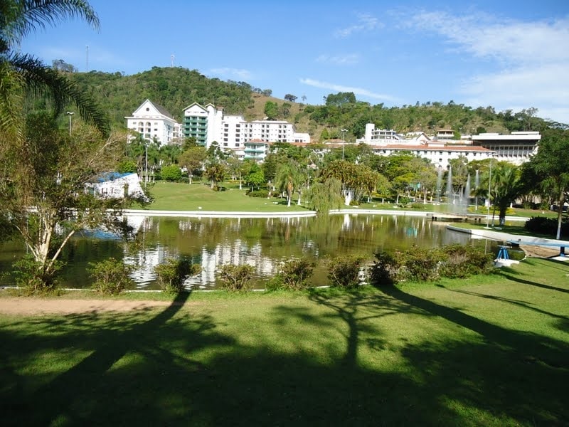 Vista de um lago em Serra Negra, São Paulo, durante o dia com prédios brancos atrás.