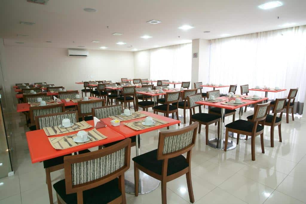 Área de refeições do Stop Way Hotel São Luís com muitas mesas e cadeiras de madeira, sob as mesas há xícaras brancas e talheres