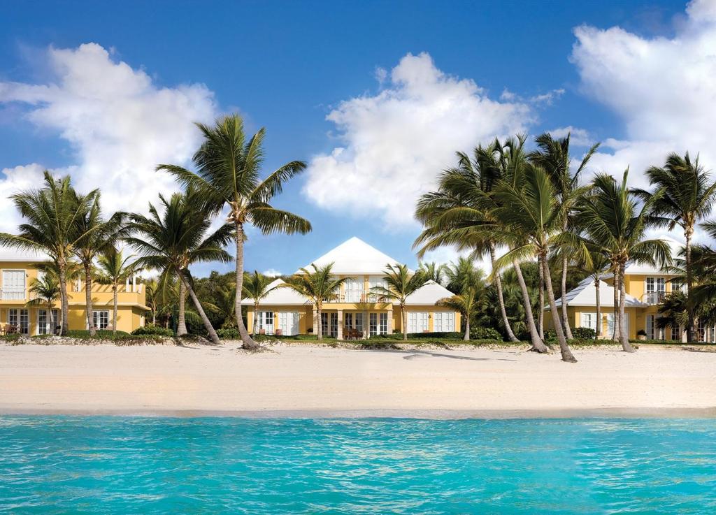 Frente de uma das acomodações do Tortuga Bay, com palmeiras na frente, areia da praia e parte do mar com água cristalina azulada. Está de dia e há nuvens brancas no céu. Imagem para ilustrar o post como escolher um resort em Punta Cana
