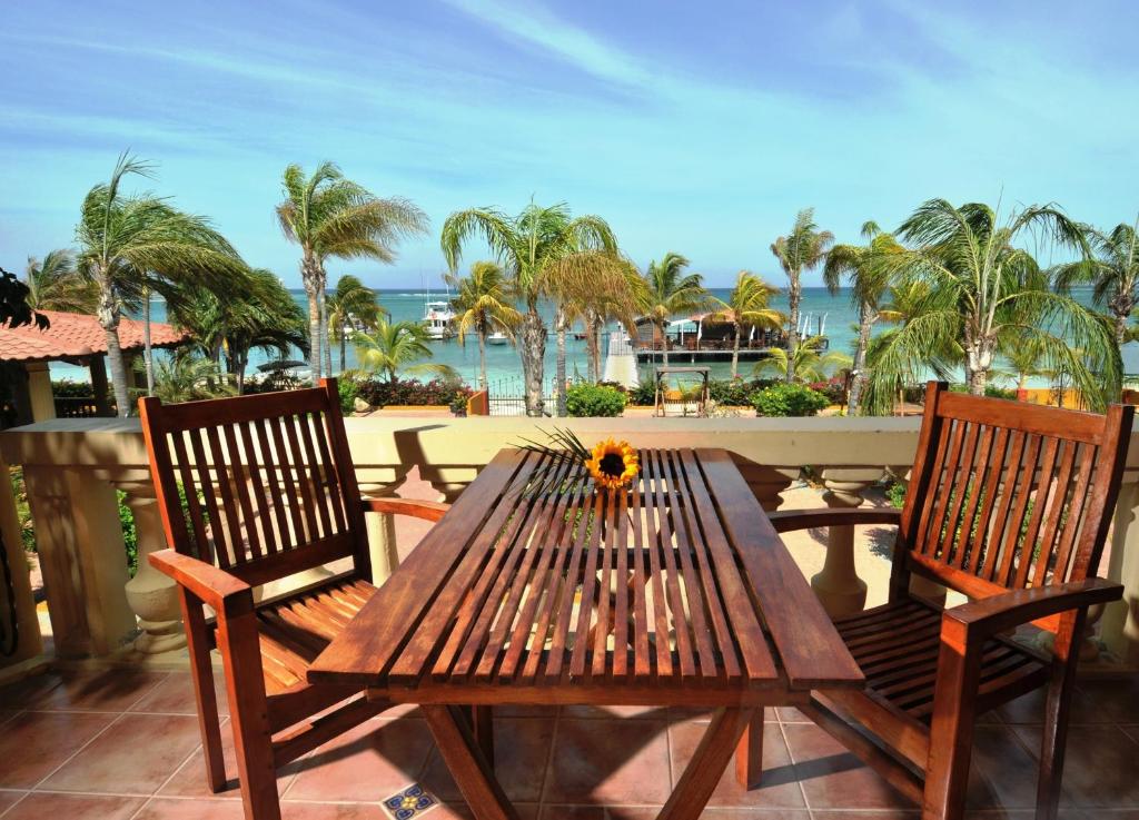 varanda do hotel Aruba Surfside Marina com uma mesa retangular de madeira e duas cadeiras, uma de cada lado da mesa. Ao fundo há várias palmeiras e o mar azul turquesa com alguns barcos.