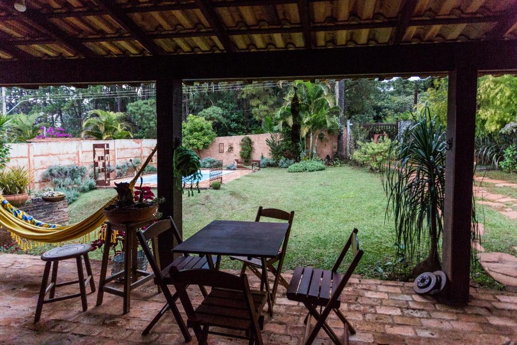 Área externa da Tiô Isolda Artes & Hospedaria, com uma varanda com mesa, cadeiras e rede e um jardim com gramado e diferentes tipos de plantas ao redor da piscina para ilustrar as pousadas em Macacos