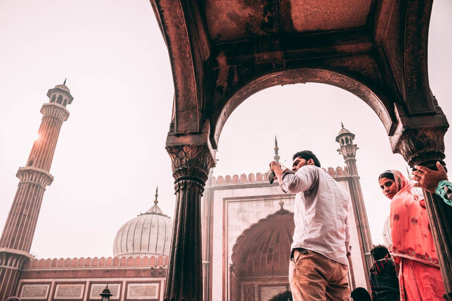 vista de baixo de algumas pessoas em Jama Masjid, em Nova Déli, um homem está tirando foto do templo que tem motivos indianos em tons de branco e amarronzado terra, para ilustrar o post de chip celular Índia