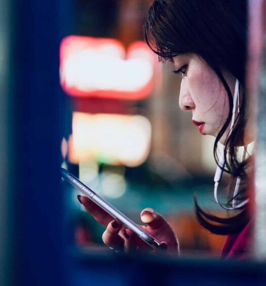 Foto bem próximo do rosto de uma mulher mexendo no celular em Shibuya, Tóquio, com algumas paredes com escritos, para ilustrar o post de chip celular Japão