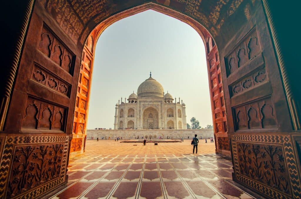 vista do Taj Mahal, em Agra a partir de um portal com inscrições e pessoas para além dele observando o imponente mausoléu em estilo indiano, ricamente trabalhado, para ilustrar o post de chip celular Índia