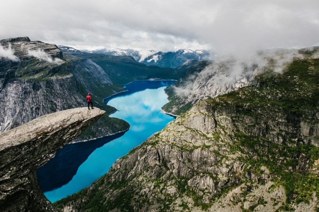 uma pessoa de pé observando um fiorde com montanhas e um rio translúcido com céu cheio de nuvens, para ilustrar o post de chip celular Noruega