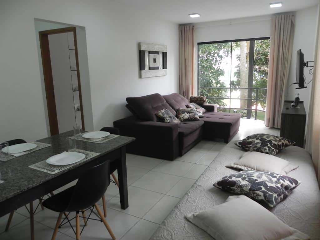 Sala de estar do Aconchego e Requinte no Centro com sofá, varanda, televisão, mesa com quatro lugares e uma cama de solteiro com almofadas