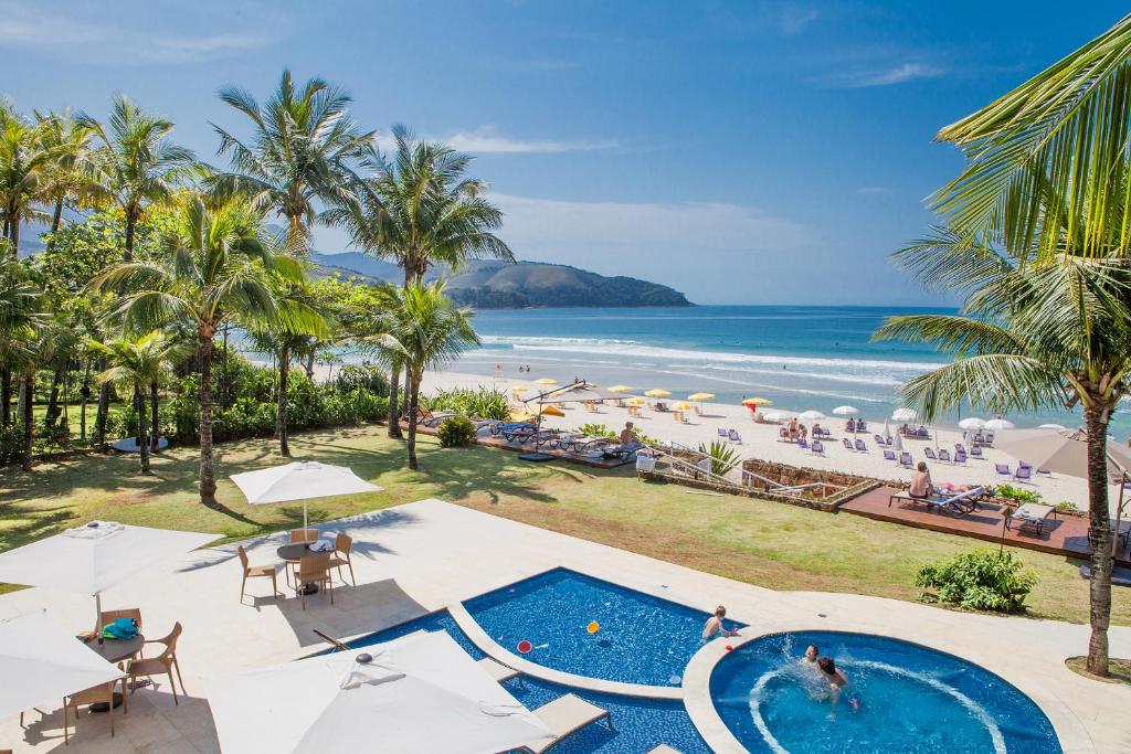 Piscina do Amora Hotel com vista direta para a praia e o mar, nos arredores da piscina há algumas árvores e um gramado, para representar pousadas pé na areia em Maresias