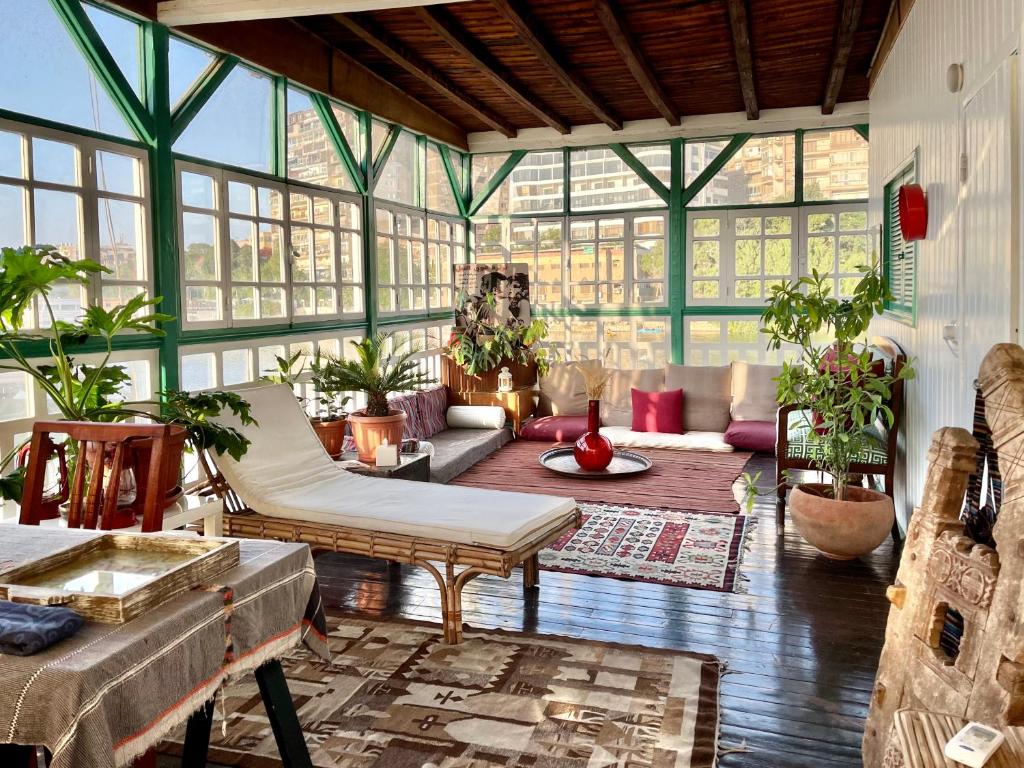 Vista da sala de estar do Houseboat65 - Historic home on the Nile durante o dia com almofadas no chão, cadeira bege e várias plantas espalhadas no ambiente.